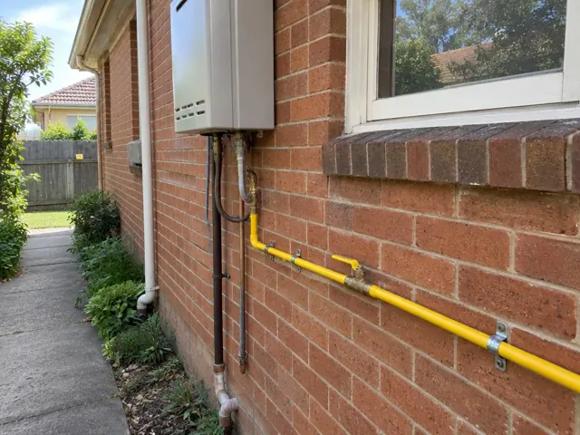 Yellow gas pipe and fittings on a brick house wall beside a window in Balgowlah
