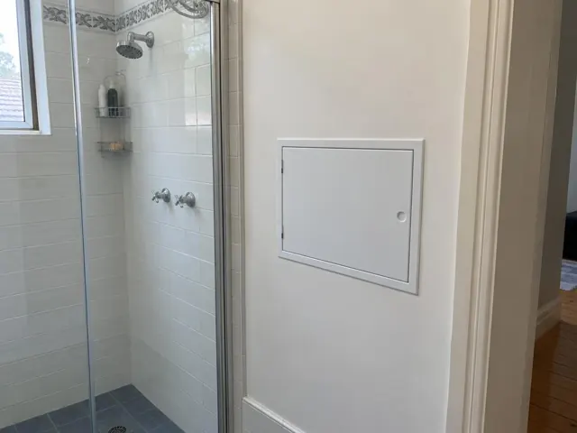 Neat access panel on a painted bathroom wall beside a tiled shower in Fairlight